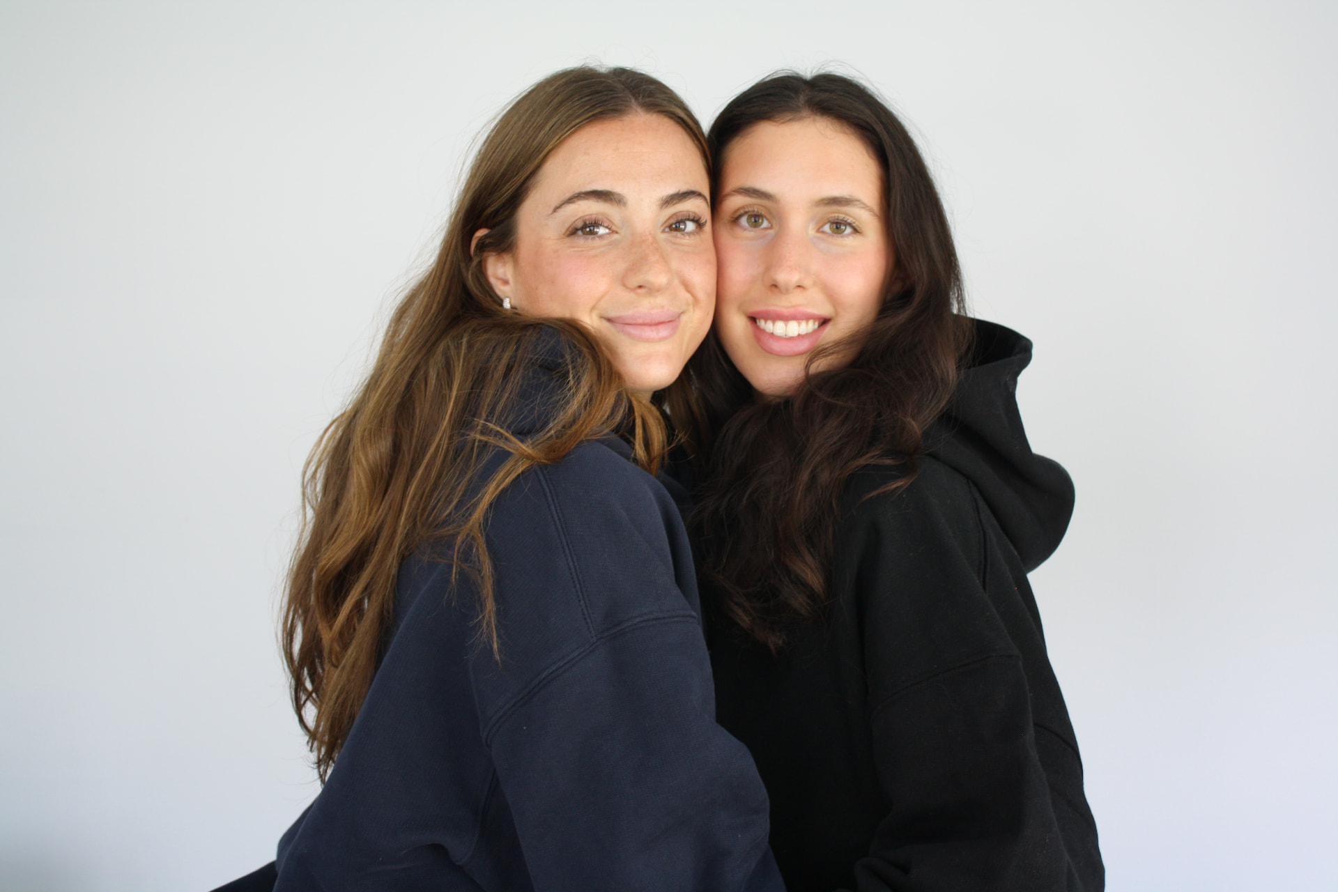 Two models wearing navy and black DMK Studios hoodies against a clean white backdrop